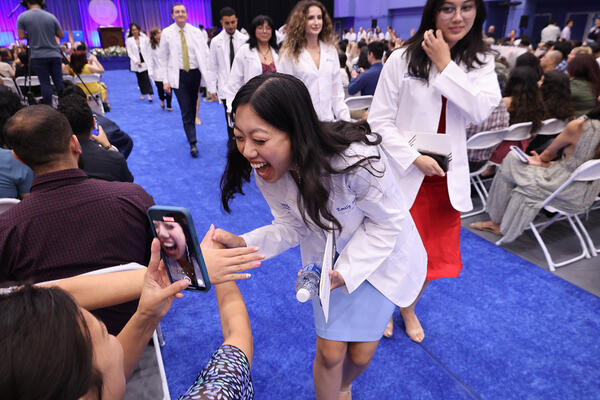 Student at white coat yelling happily into a phone